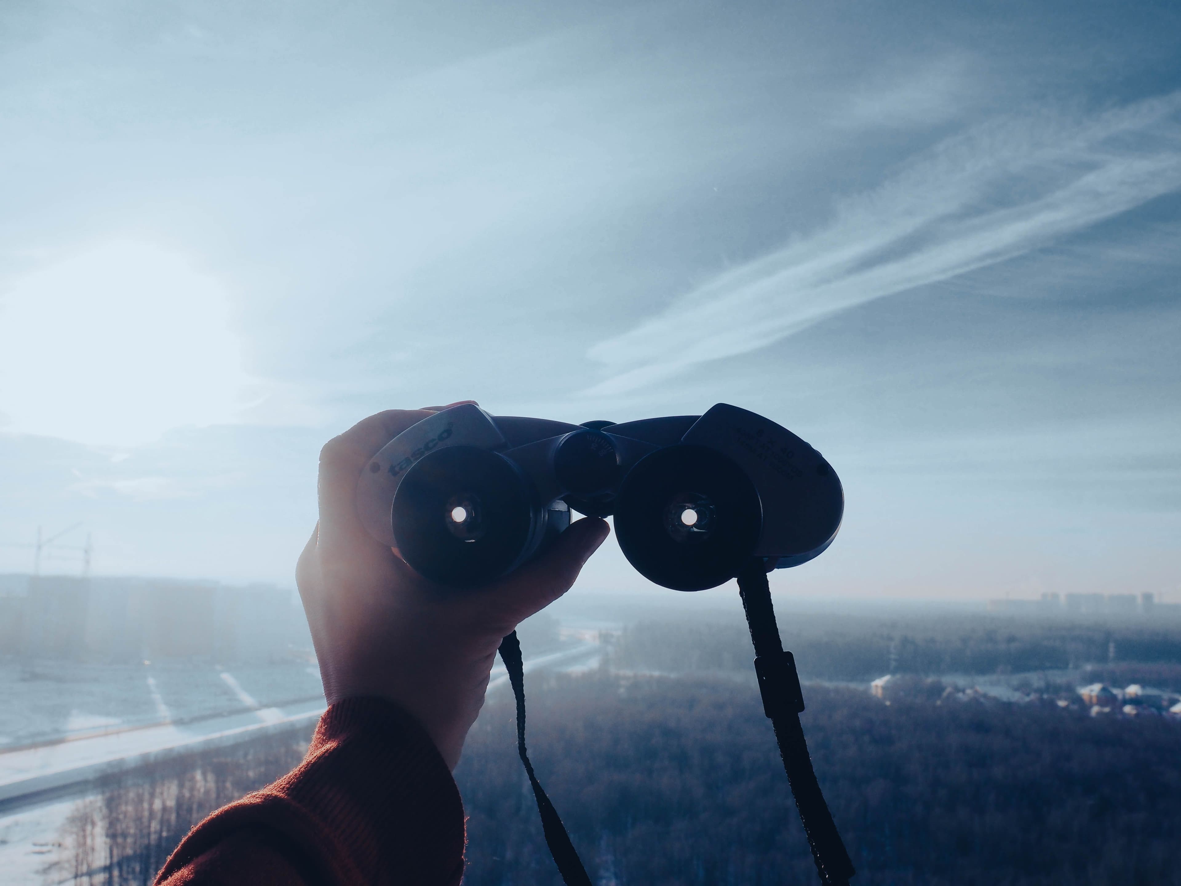 A person looking through binoculars against an open sky.